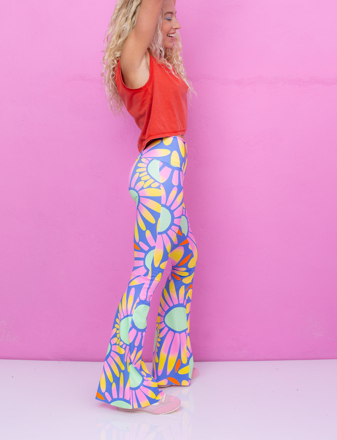 A woman wearing an orange tank top and colourful flower pattern high wasted flares
