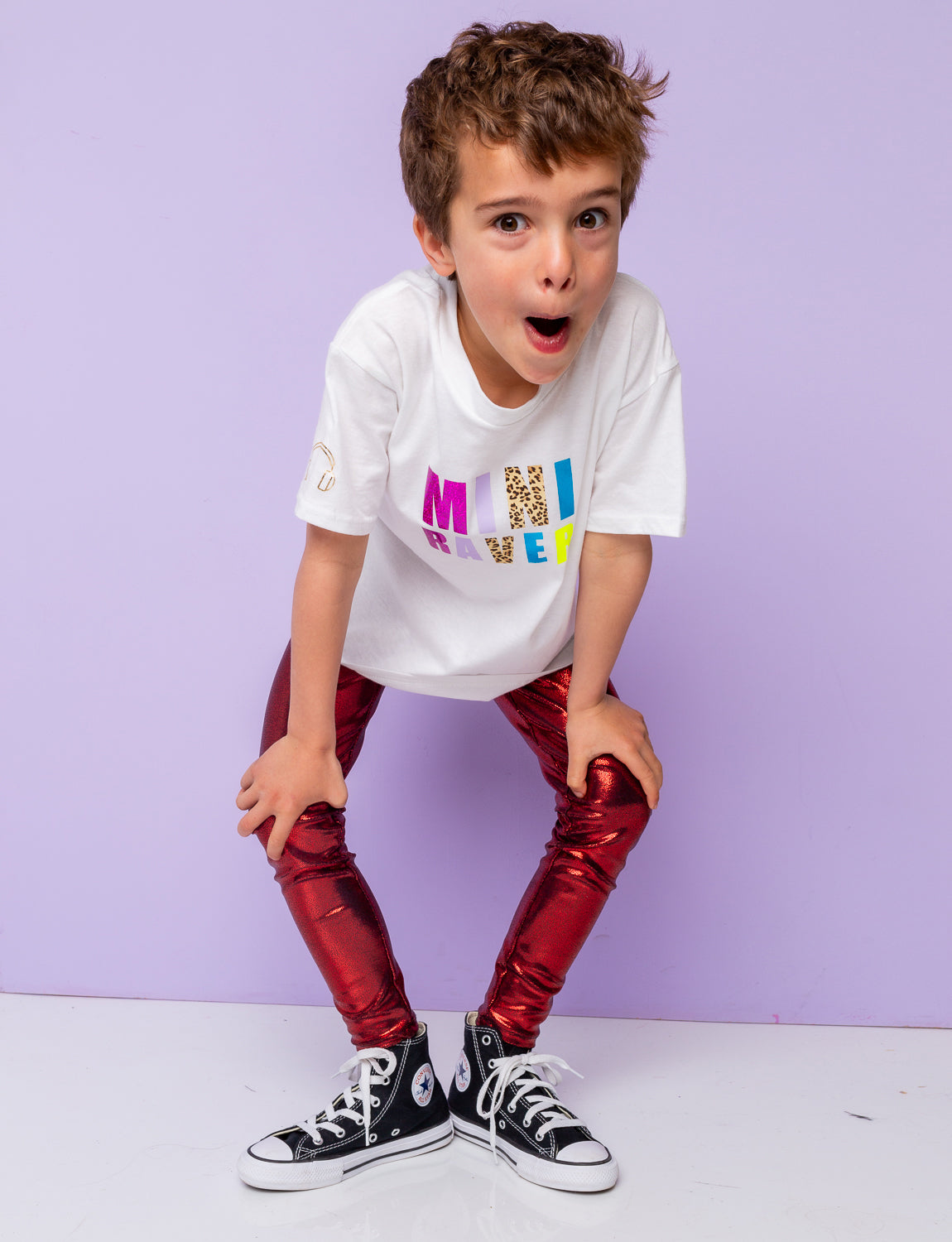 Boy modelling metallic red leggings and a white t-shirt with balck Converse trainers.