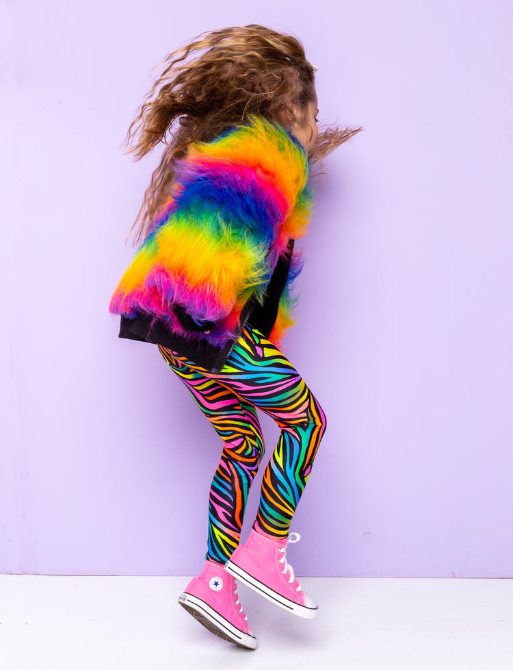 Girl jumping in the air modelling rainbow zebra print leggings with a rainbow fur jacket.