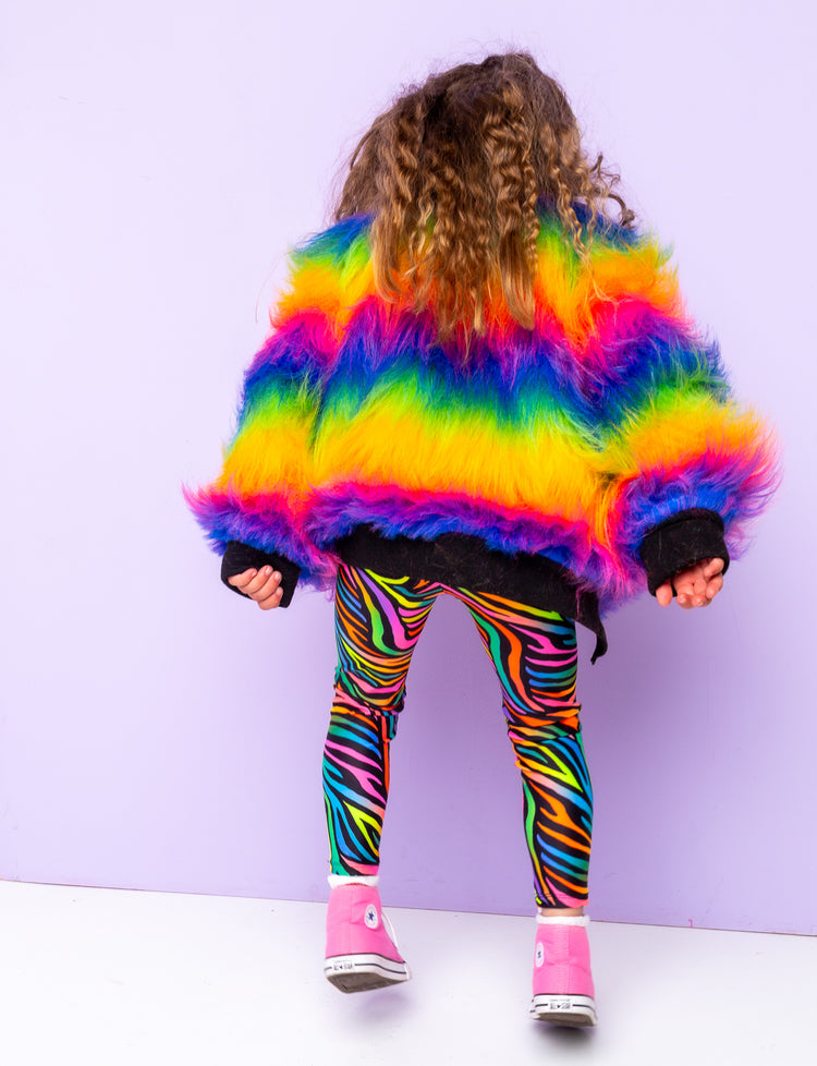 Back view of a girl modelling rainbow zebra print leggings with a rainbow fur jacket.