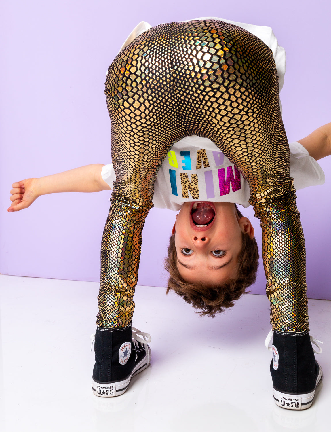 Boy upside down look through his legs wearing gold holographic snakeskin leggings.