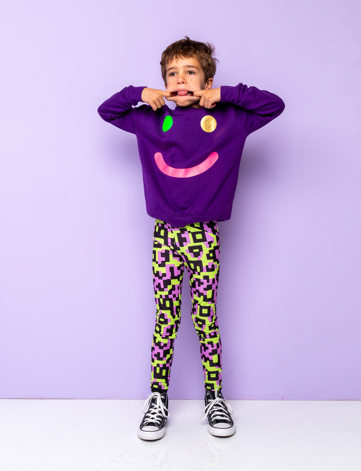 Boy wearing patterned leggings with a purple smily sweatshirt.