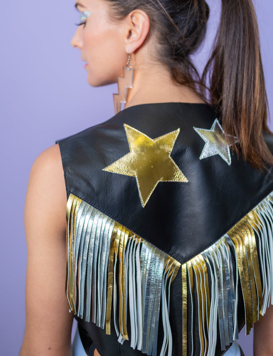 The image shows the back of a woman wearing a black leather waistcoat jacket with gold and silver fringe and applique stars.