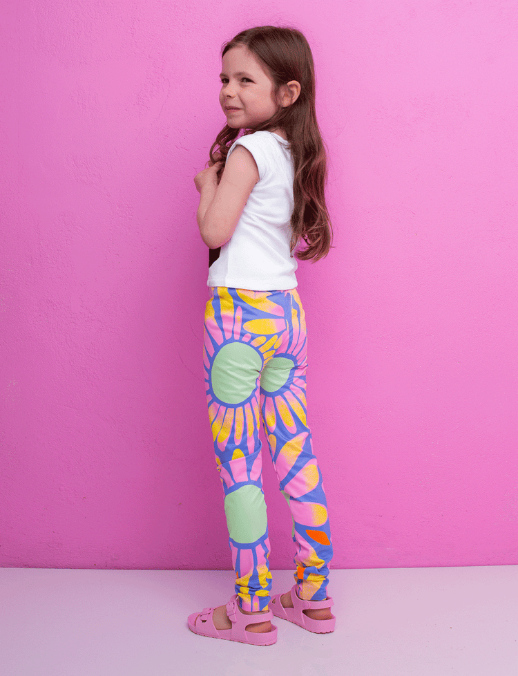 Young girl wearing colorful tie-dye leggings against a pink background