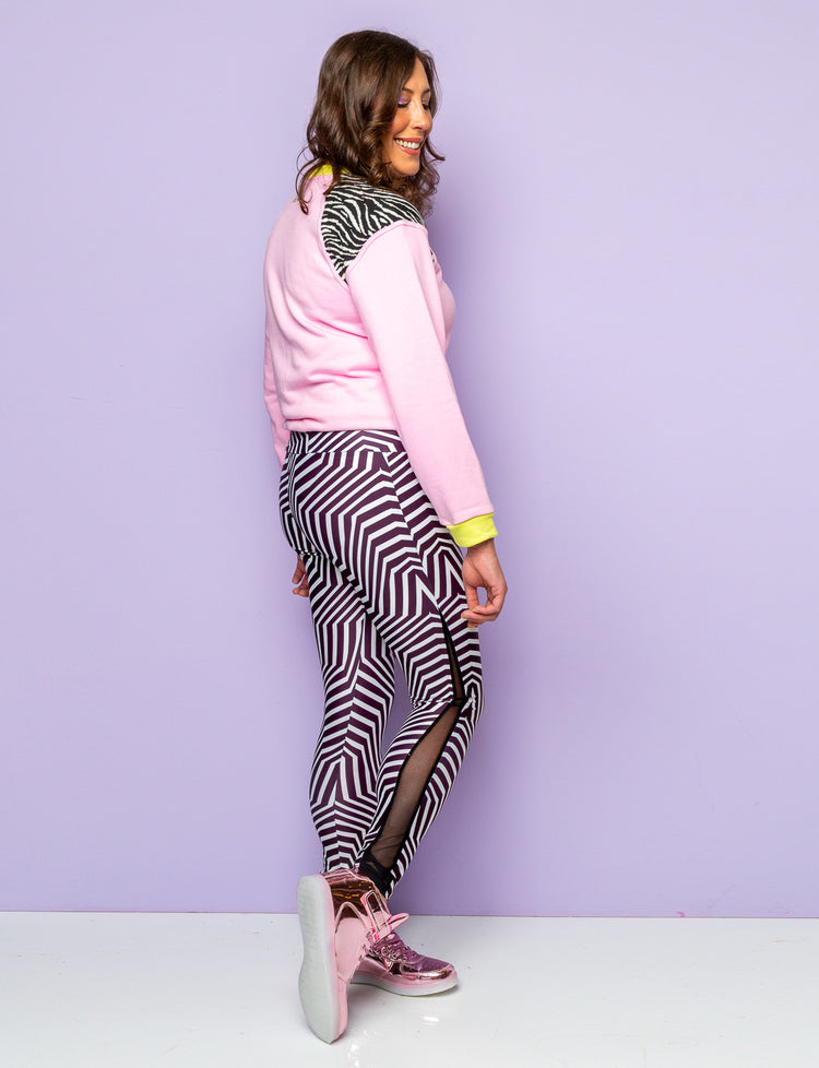 Side view of a woman wearing psychedelic black and white printed leggings and a pink and zebra print sweatshirt. 