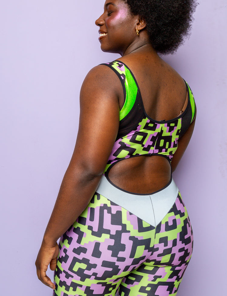 Back view of a woman wearing a lilac and lime green patterned lycra catsuit with peekaboo back detail.