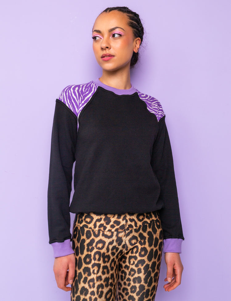 woman wearing a black sweatshirt with purple zebra print shoulders tucked under at the hips
