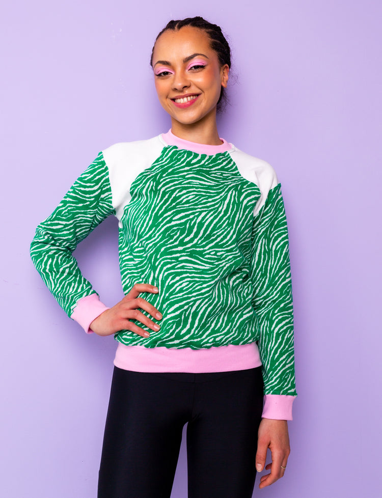 Woman wearing a green zebra print sweatshirt with pink and white panels.