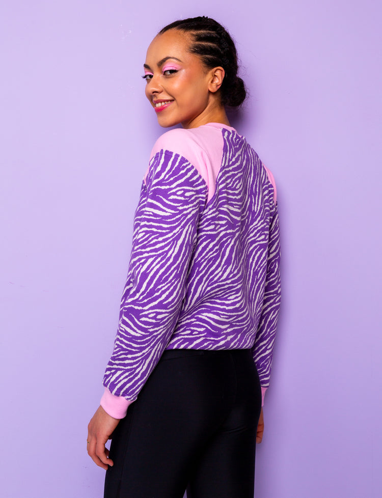 side view of a woman wearing a purple zebra print sweatshirt with pink shoulders 