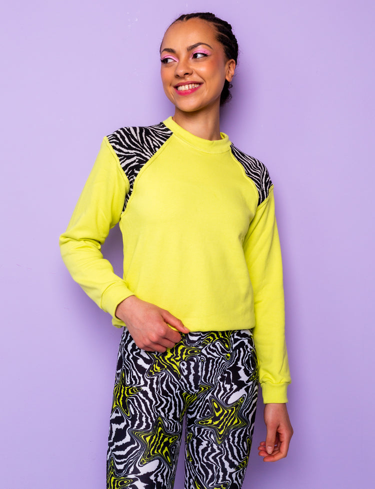 woman wearing a lime green sweatshirt with black and white zebra print shoulders tucked under at the hips