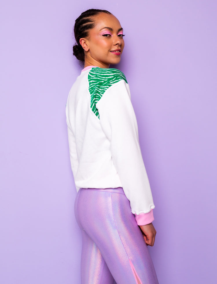 side view of a woman wearing a white sweatshirt with green zebra print shoulders tucked under at the hips