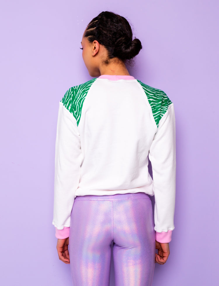 back view of a woman wearing a white sweatshirt with green zebra print shoulders tucked under at the hips