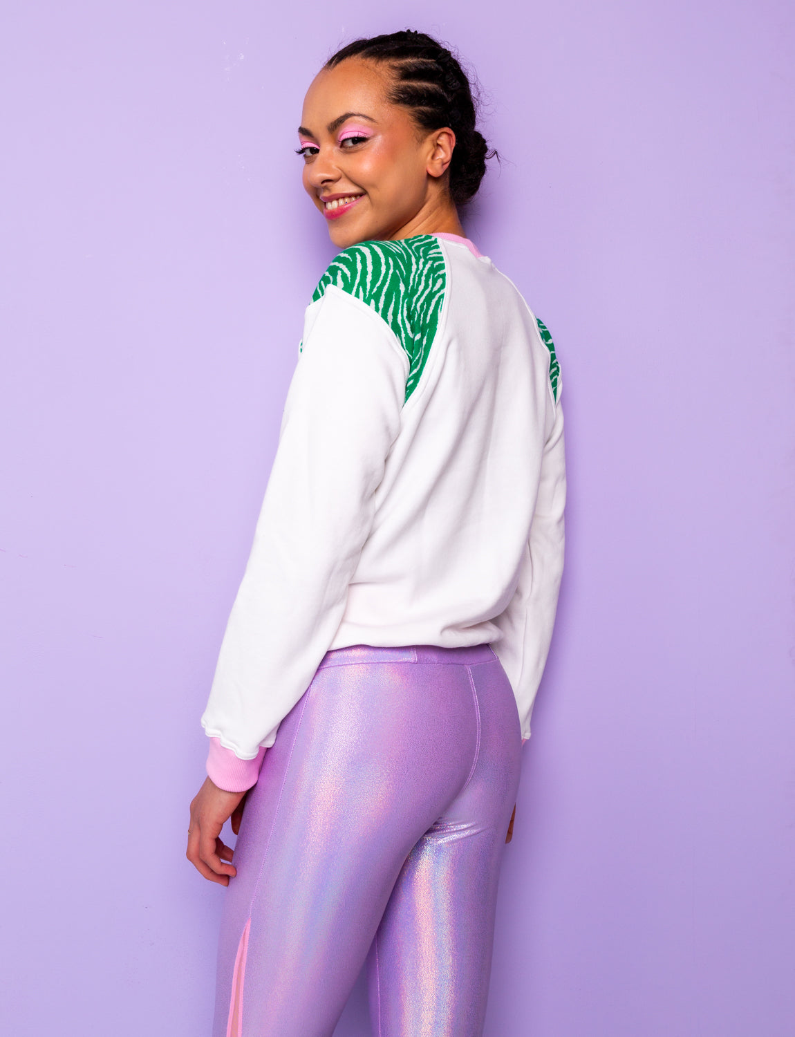 woman wearing a white sweatshirt with green zebra print shoulders tucked under at the hips with shiny lilac leggings