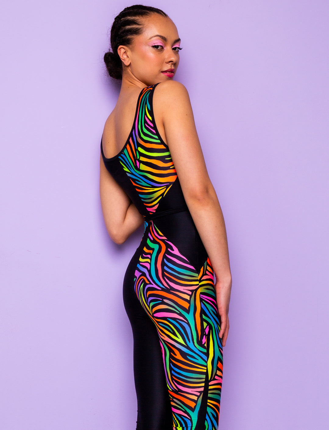Side view of a woman wearing a printed lycra catsuit with rainbow zebra print and contrasting black panels.