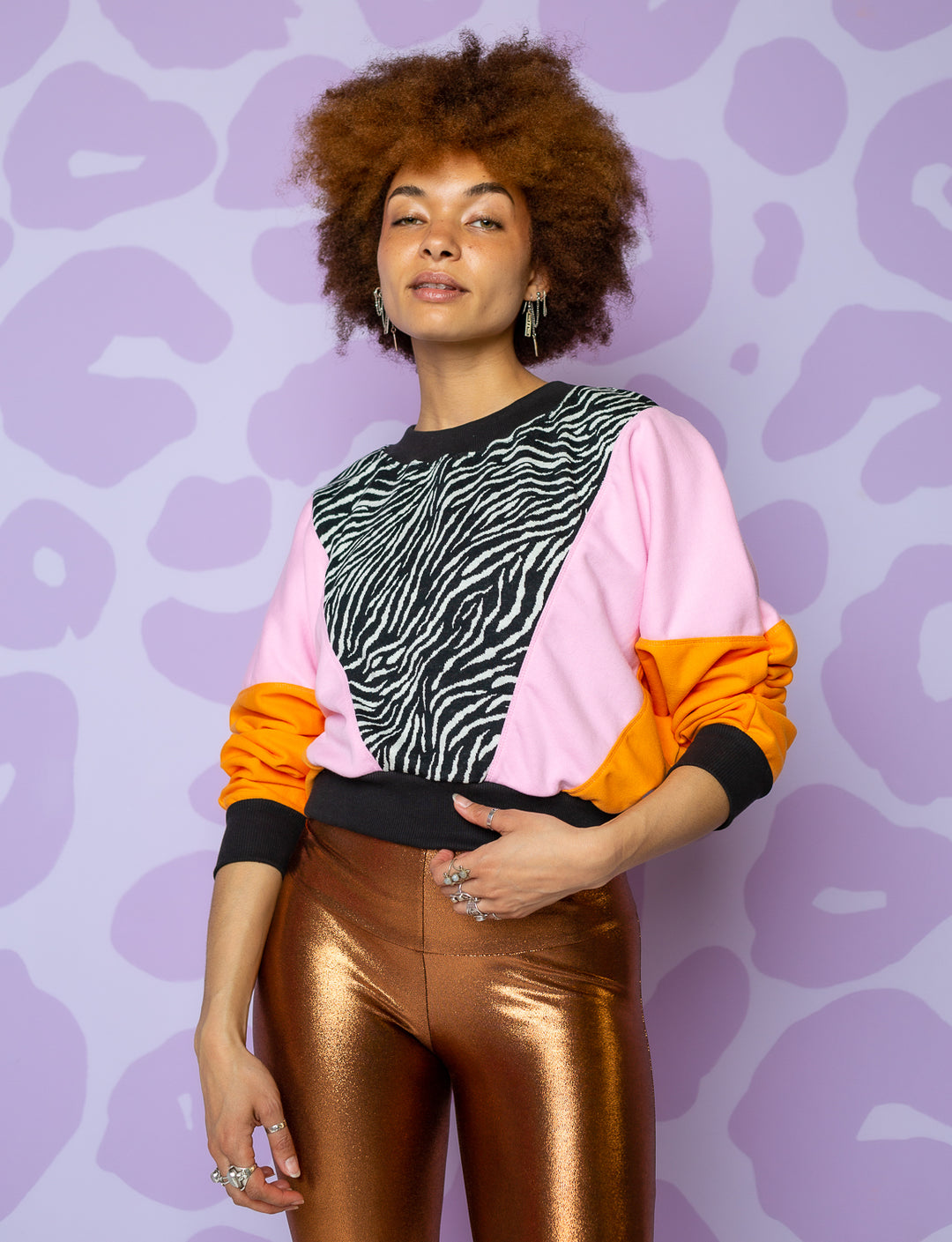 woman wearing crop sweatshirt with orange sleeves, pink panel on body and black and white zebra panel in front with black neck, hem and cuffs