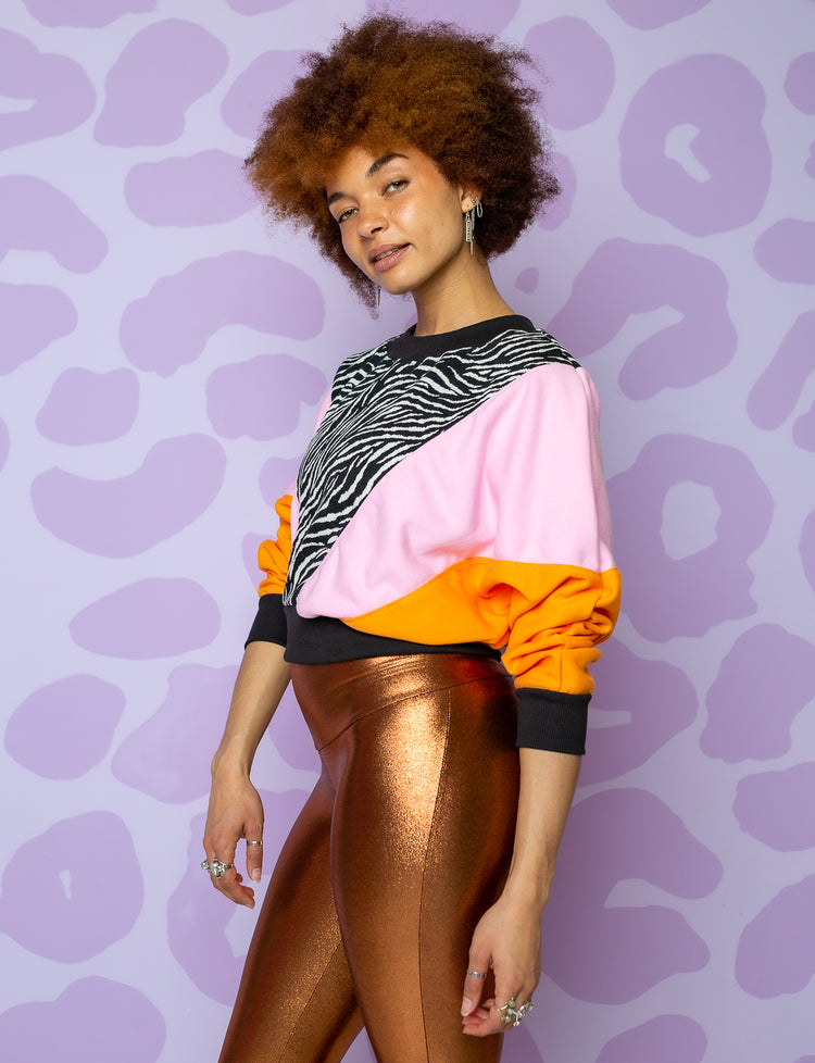 woman wearing crop sweatshirt with orange sleeves, pink panel on body and black and white zebra panel in front with black neck, hem and cuffs