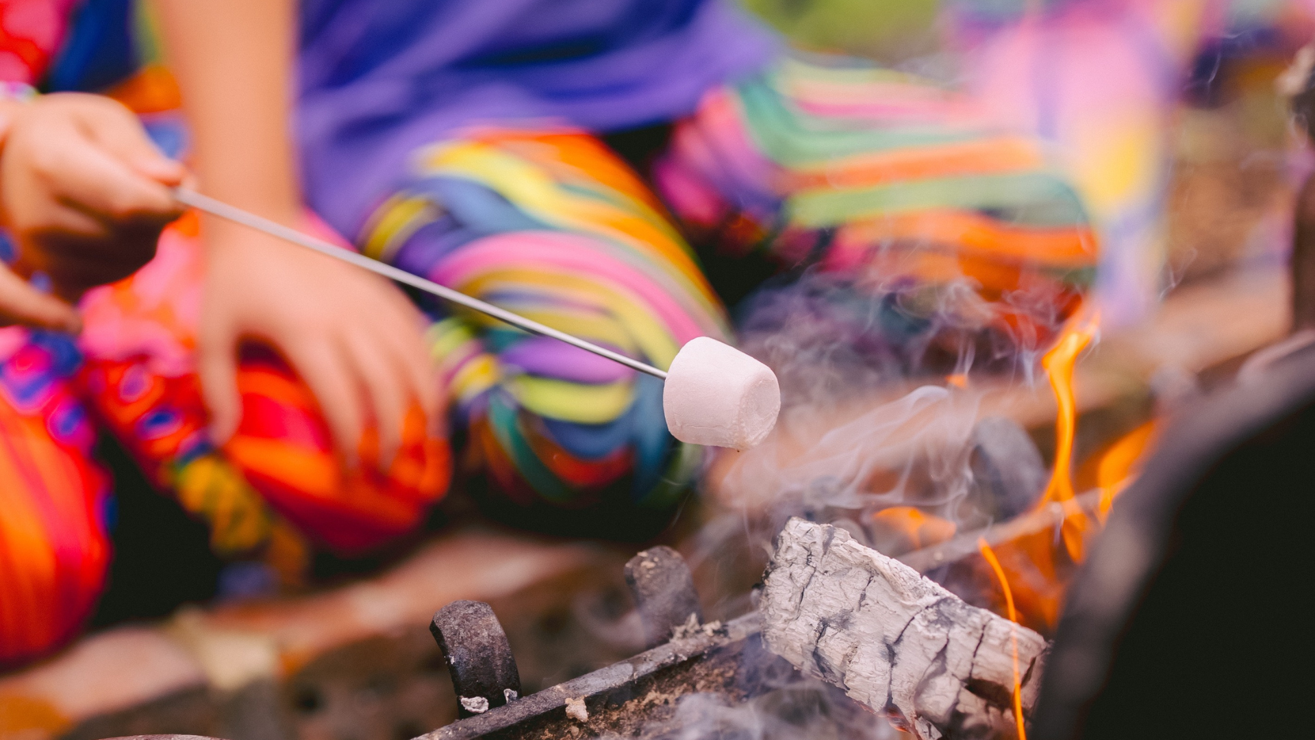Person roasting marshmallows over a campfire with colorful pants.