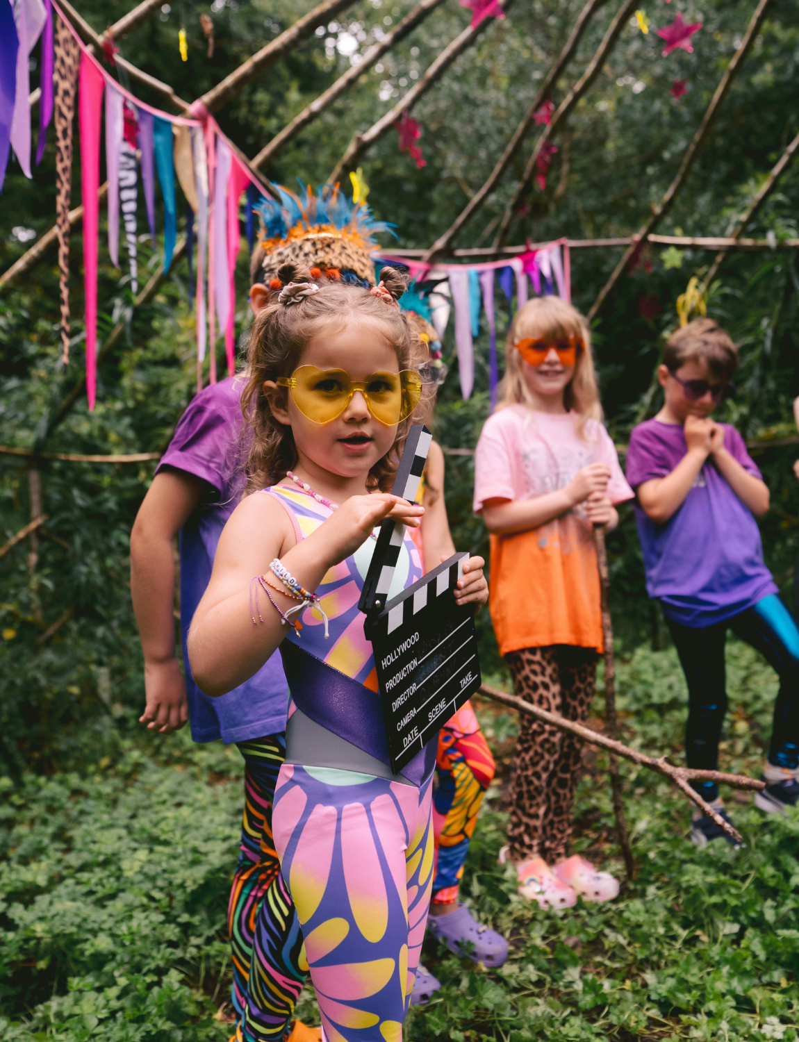 Children in colorful outfits with a clapperboard outdoors
