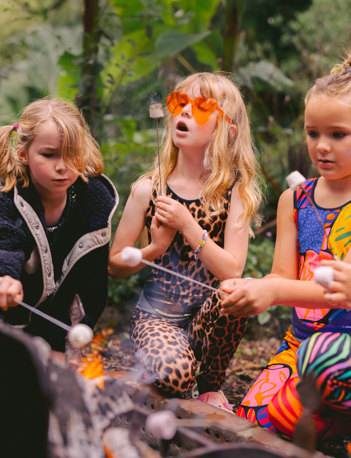 Three children roasting marshmallows over a campfire in a forest setting.