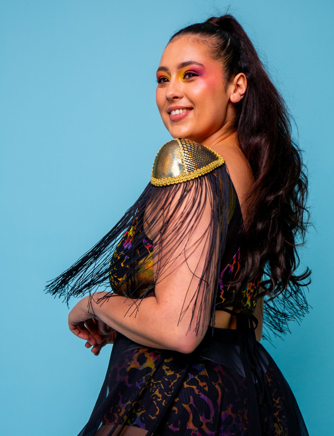 Woman wearing a colorful outfit with a gold shoulder piece against a blue background