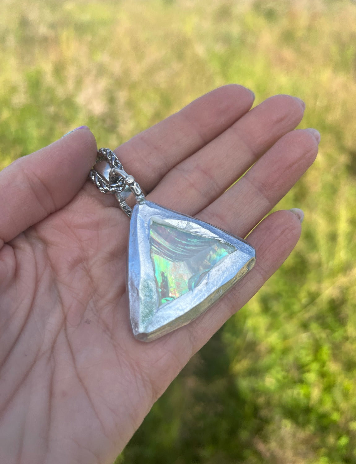 a triangle iridescent angel aura quartz necklace is lying in a ladies hand