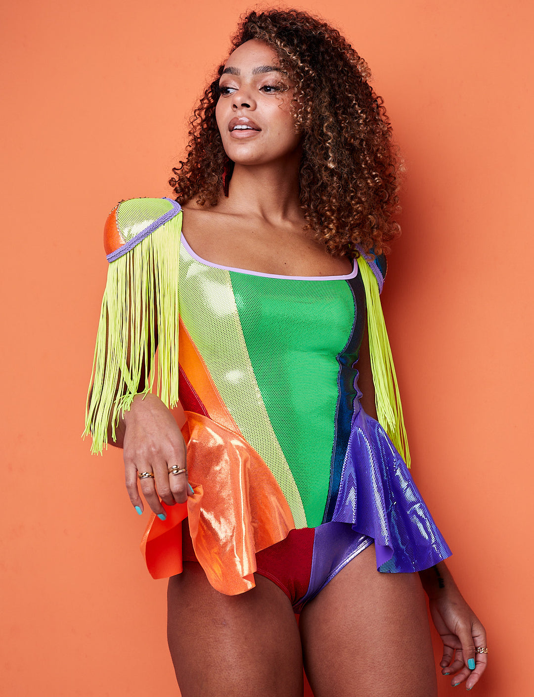 A model wearing rainbow shoulder pads that have yellow fringing. The model is wearing a matching rainbow bodysuit 
