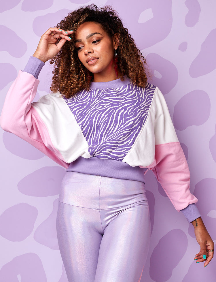 A model wearing a burnt soul cropped sweatshirt in lilac and white zebra print with pink and white panels and wearing lilac leggings