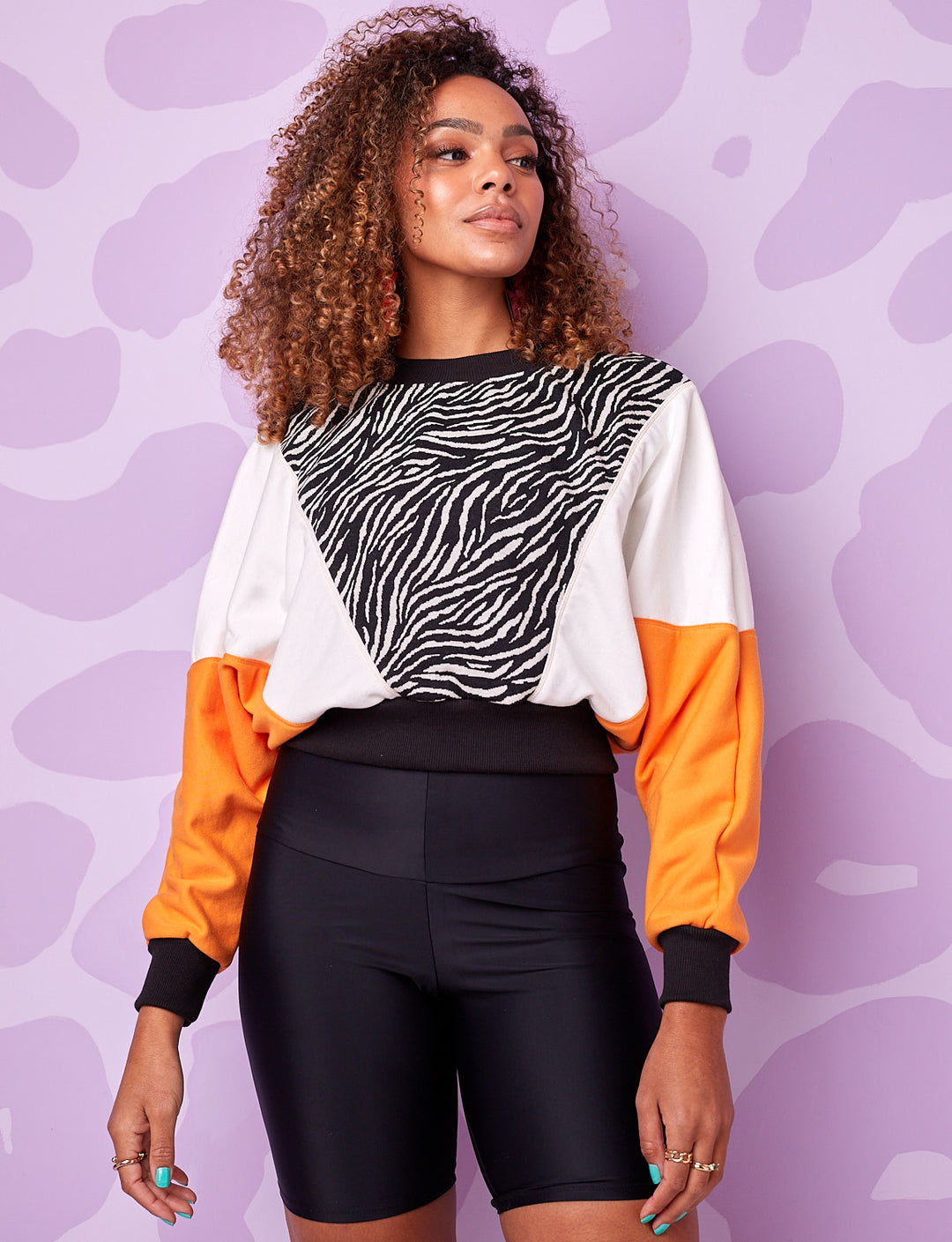 A model wearing a burnt soul cropped sweatshirt in black and white zebra print with orange and black panels and wearing black cycling shorts